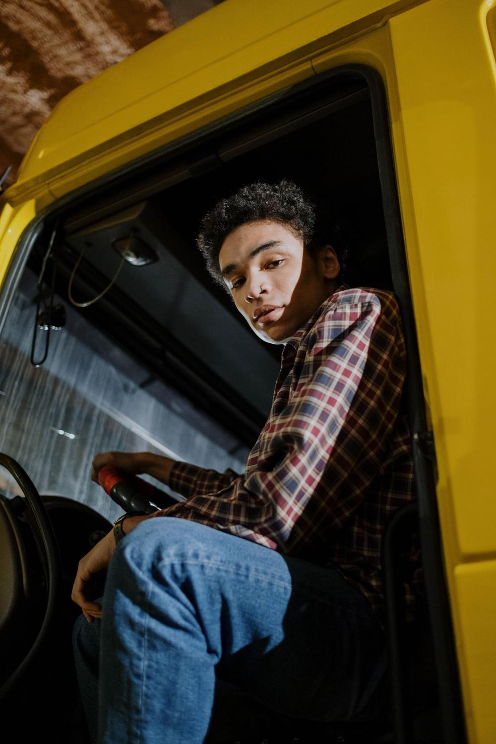 Un om urcă în cabina unui camion galben și se uită înapoi, peste umăr.