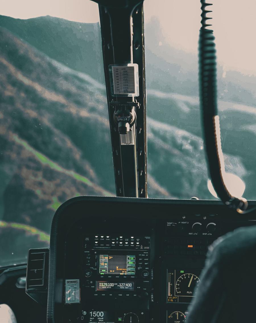 Din carlinga unui elicopter în zbor: parbrizul cu versanți împăduriți în ceață, dedesubt panoul cu radioul și instrumentele