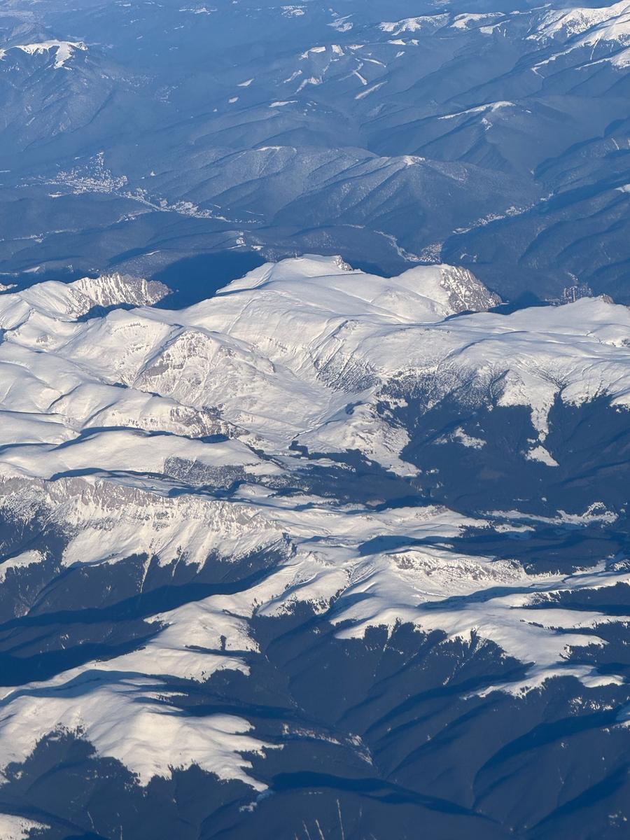 Carpații iarna, fotografiați din avion: culmi albe de zăpadă și văi întunecate