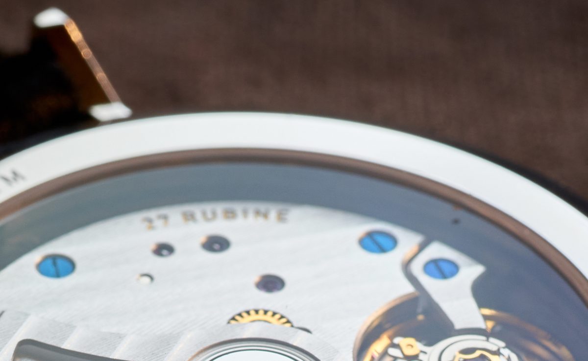 Macro photograph of a dress watch movement with blue steel screws and a partial gold rotor