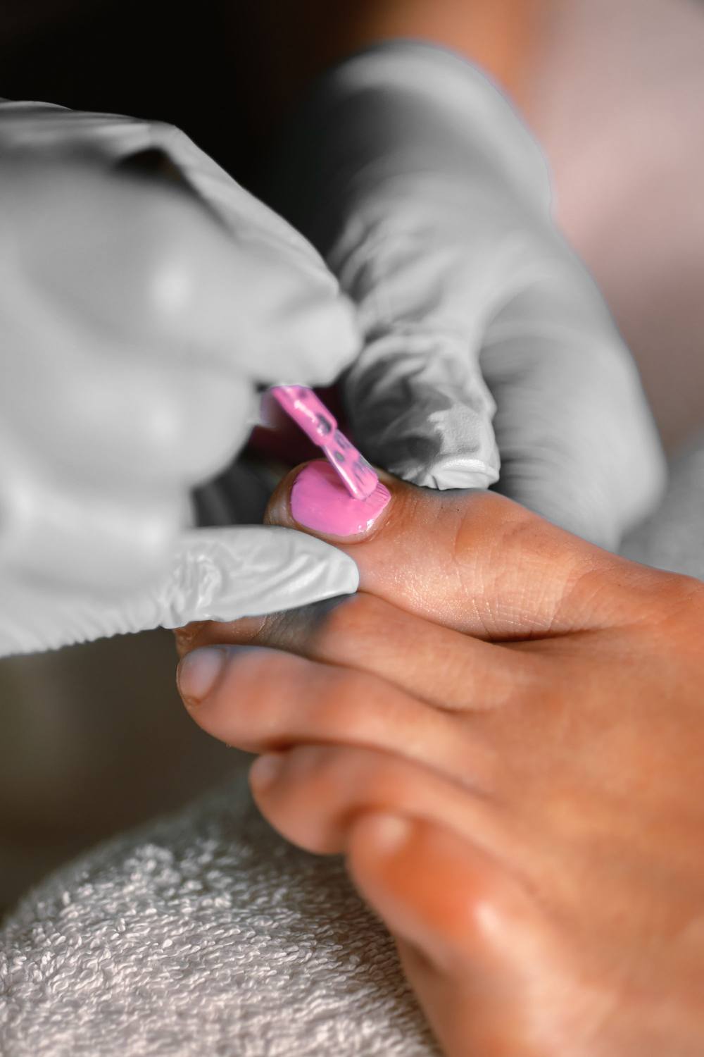 Pedichiură, de aproape: ojă roz întinsă pe unghia mare, piciorul sprijinit pe un prosop.