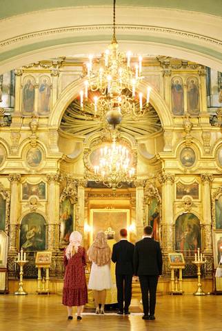 Biserica aurită cu candelabre; mirii și nașii stau în fața altarului