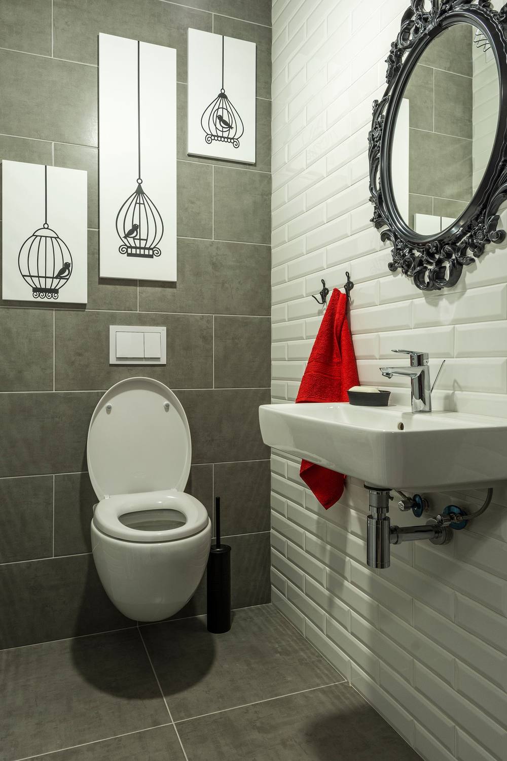 WC suspendat pe un perete cu plăci gri închis; alături, faianță albă dreptunghiulară așezată ca zidăria, sub o oglindă cu ramă neagră.