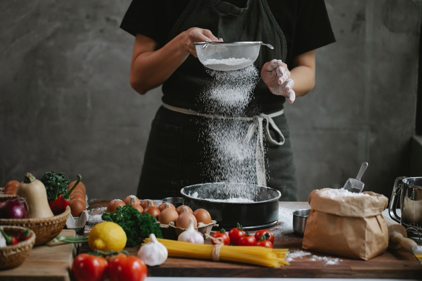 Bucătar cernând făină peste ingrediente proaspete, în bucătărie