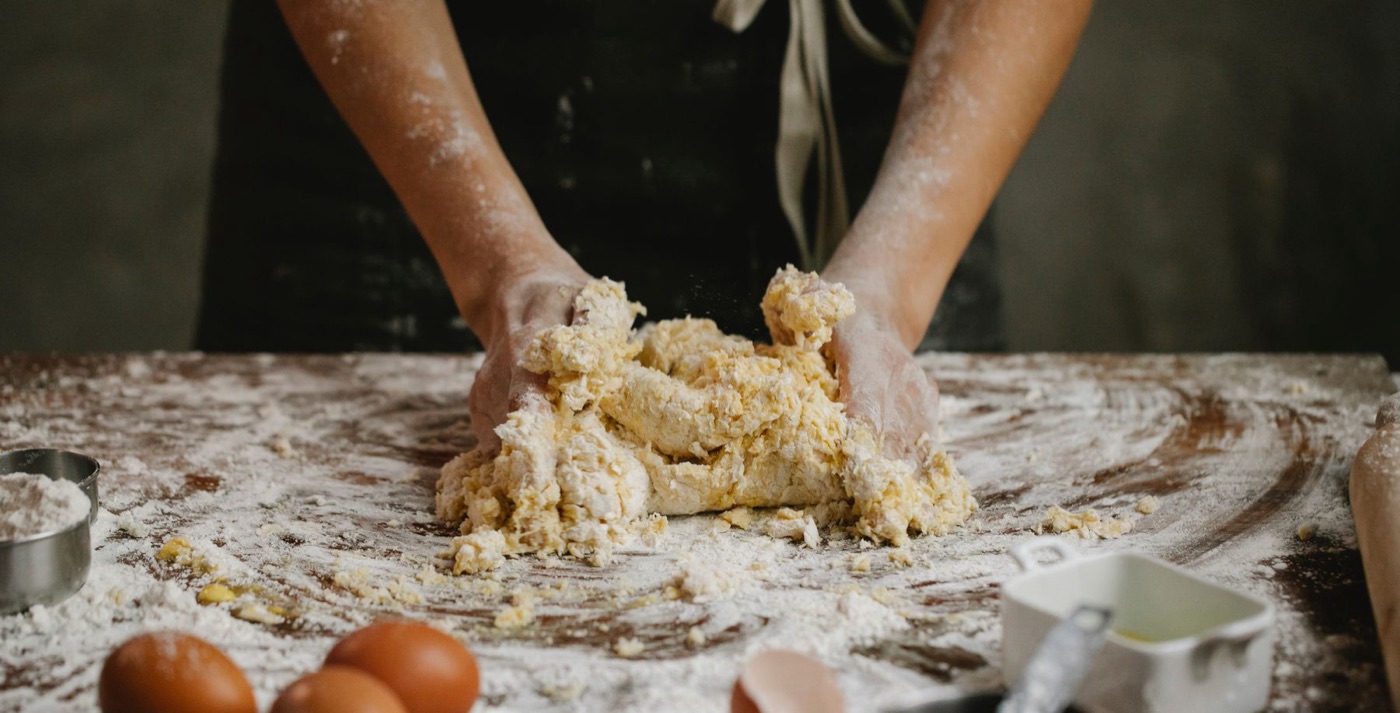 Mâini frământând aluat de pizza pe masă cu făină